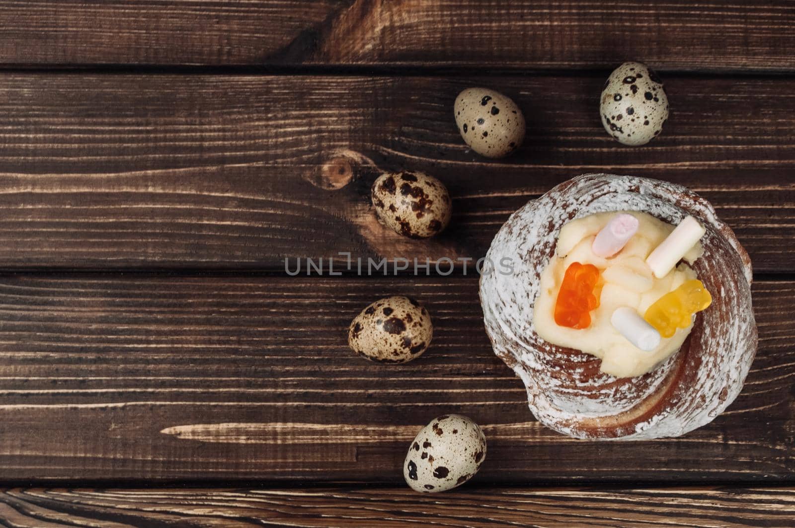Stylish Easter cake with marshmallows and jelly bears on a dark rustic wooden background, quail eggs lie nearby. Seasonal Greetings Happy Easter. copy space. view from above. modern happy easter image
