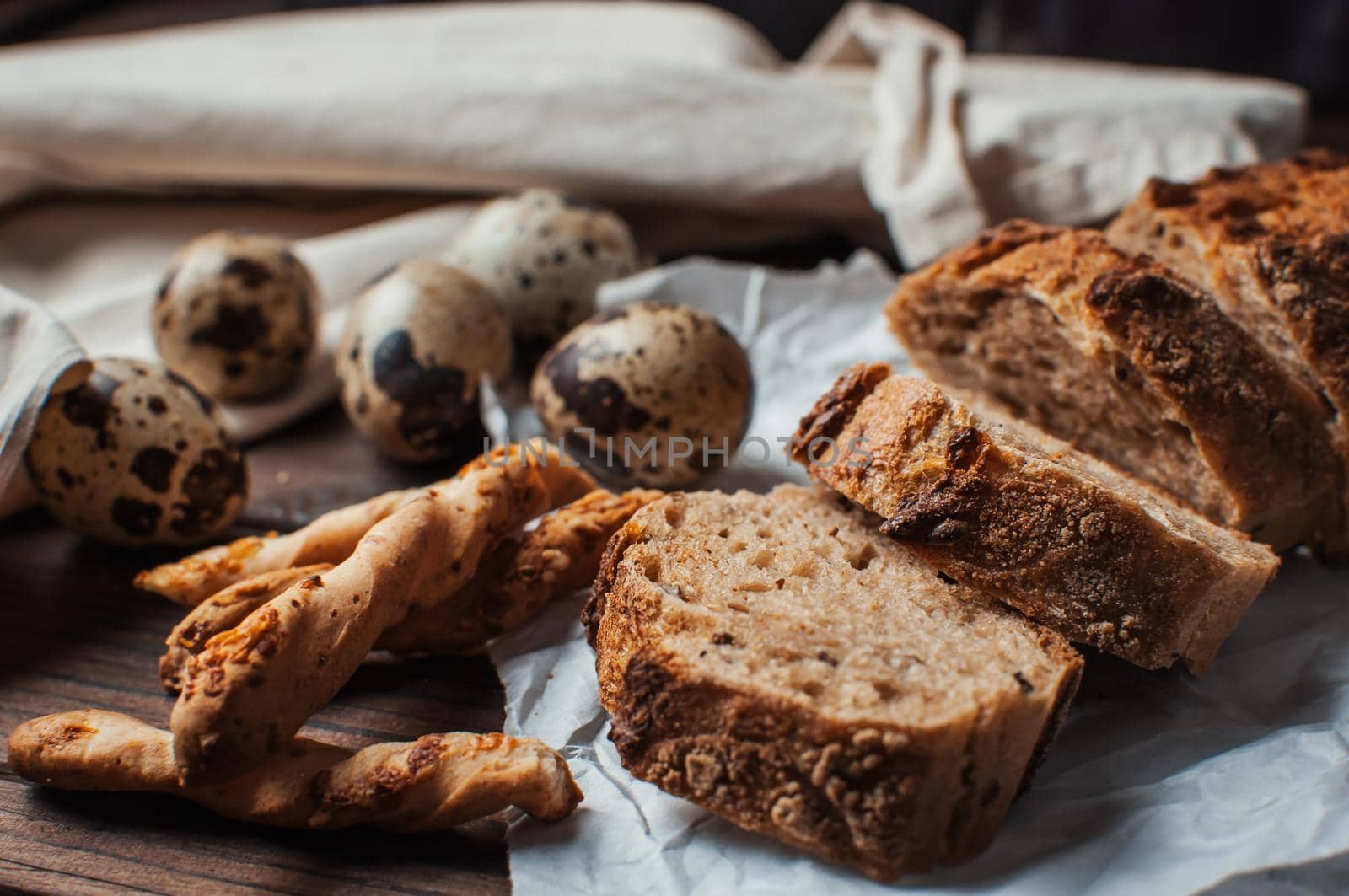 set dark yeast free buckwheat bread in a cut lies on parchment, next to quail eggs and Italian grissini. The concept of preparing breakfast.