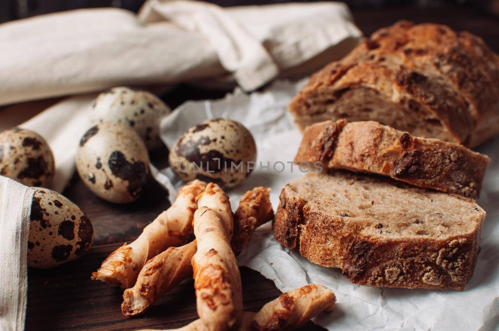 set dark yeast free buckwheat bread in a cut lies on parchment, next to quail eggs and Italian grissini. The concept of preparing breakfast.