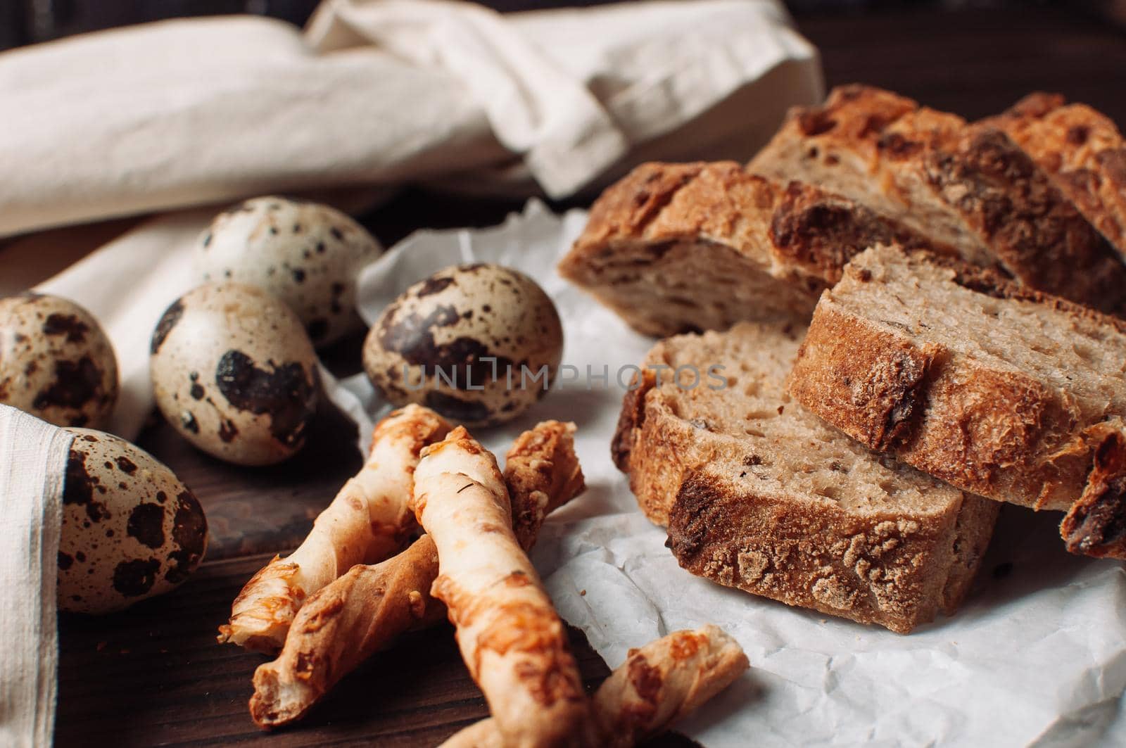 set dark yeast free buckwheat bread in a cut lies on parchment, next to quail eggs and Italian grissini. The concept of preparing breakfast.