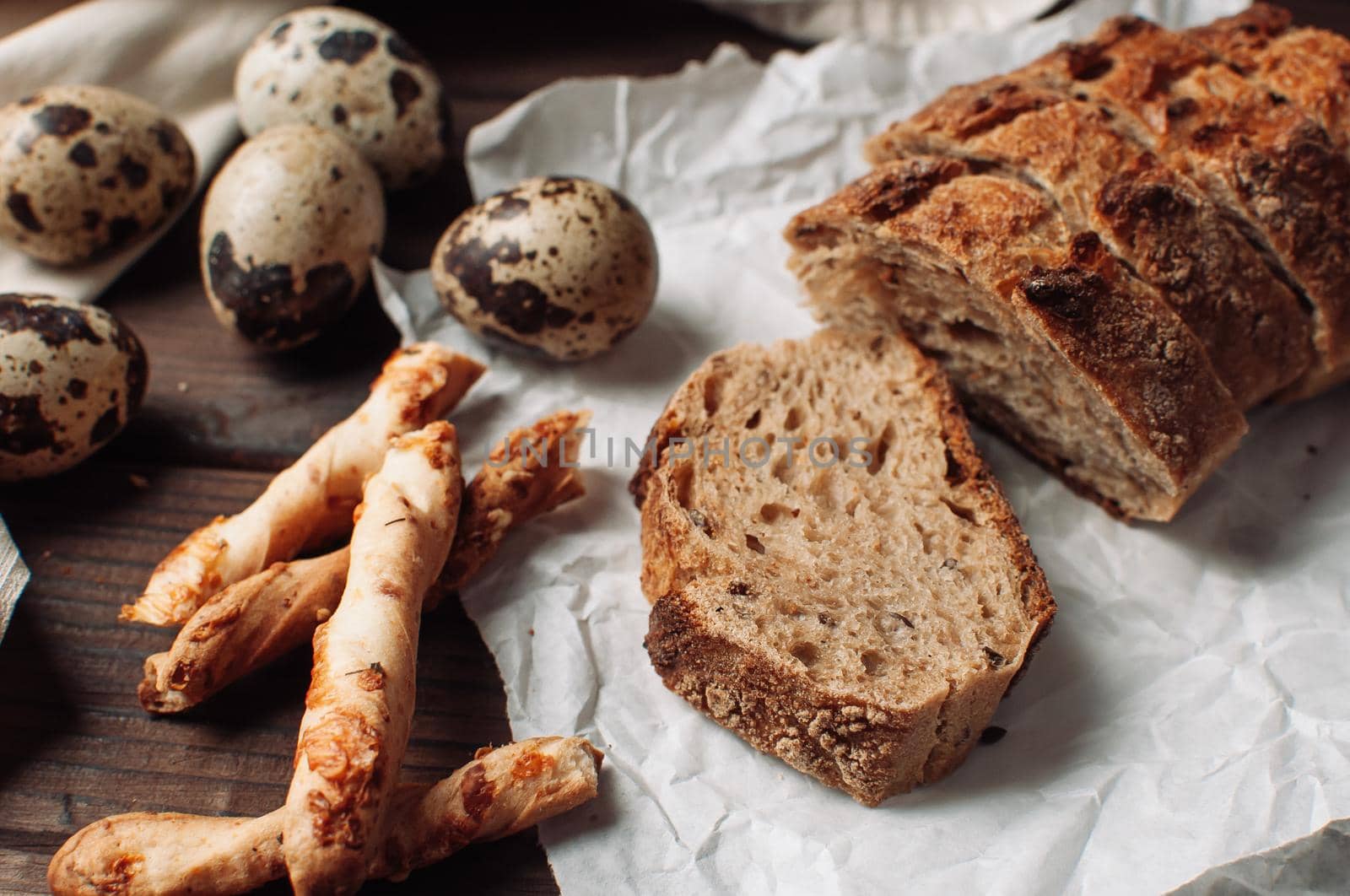 set dark yeast free buckwheat bread in a cut lies on parchment, next to quail eggs and Italian grissini. The concept of preparing breakfast.