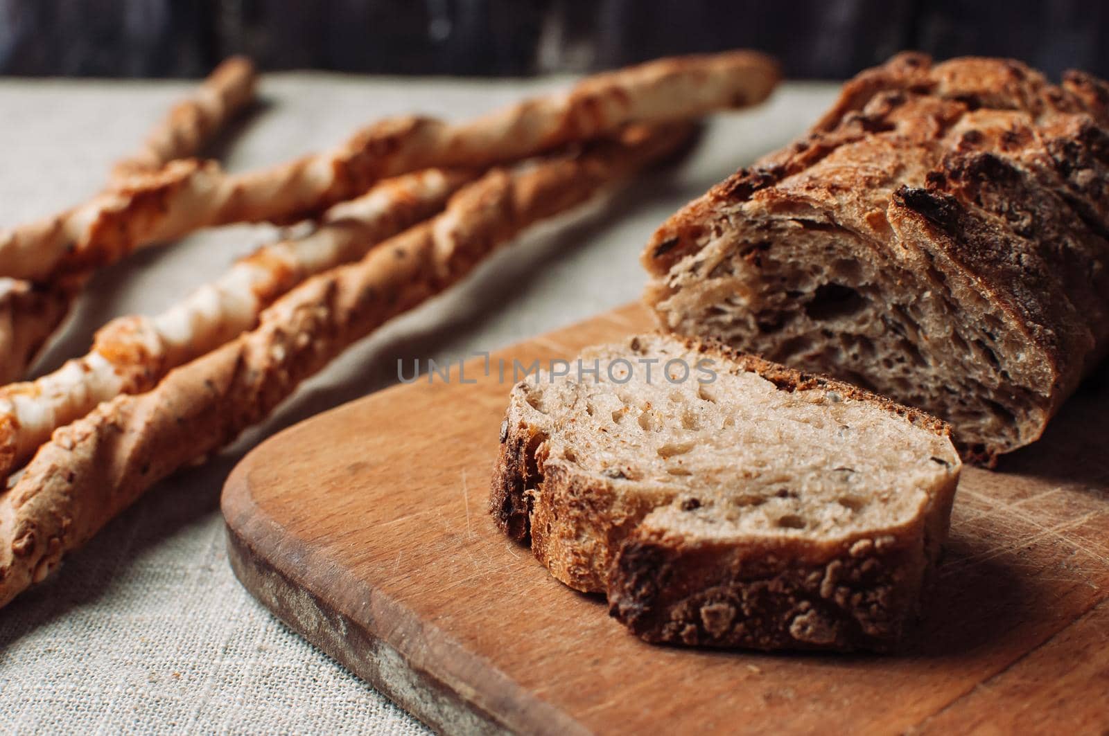 dark yeast-free buckwheat bread in a cut lies on a cutting wooden board on a wooden table, next to it is Italian grissini on a linen tablecloth in a rustic style. Breakfast cooking concept.