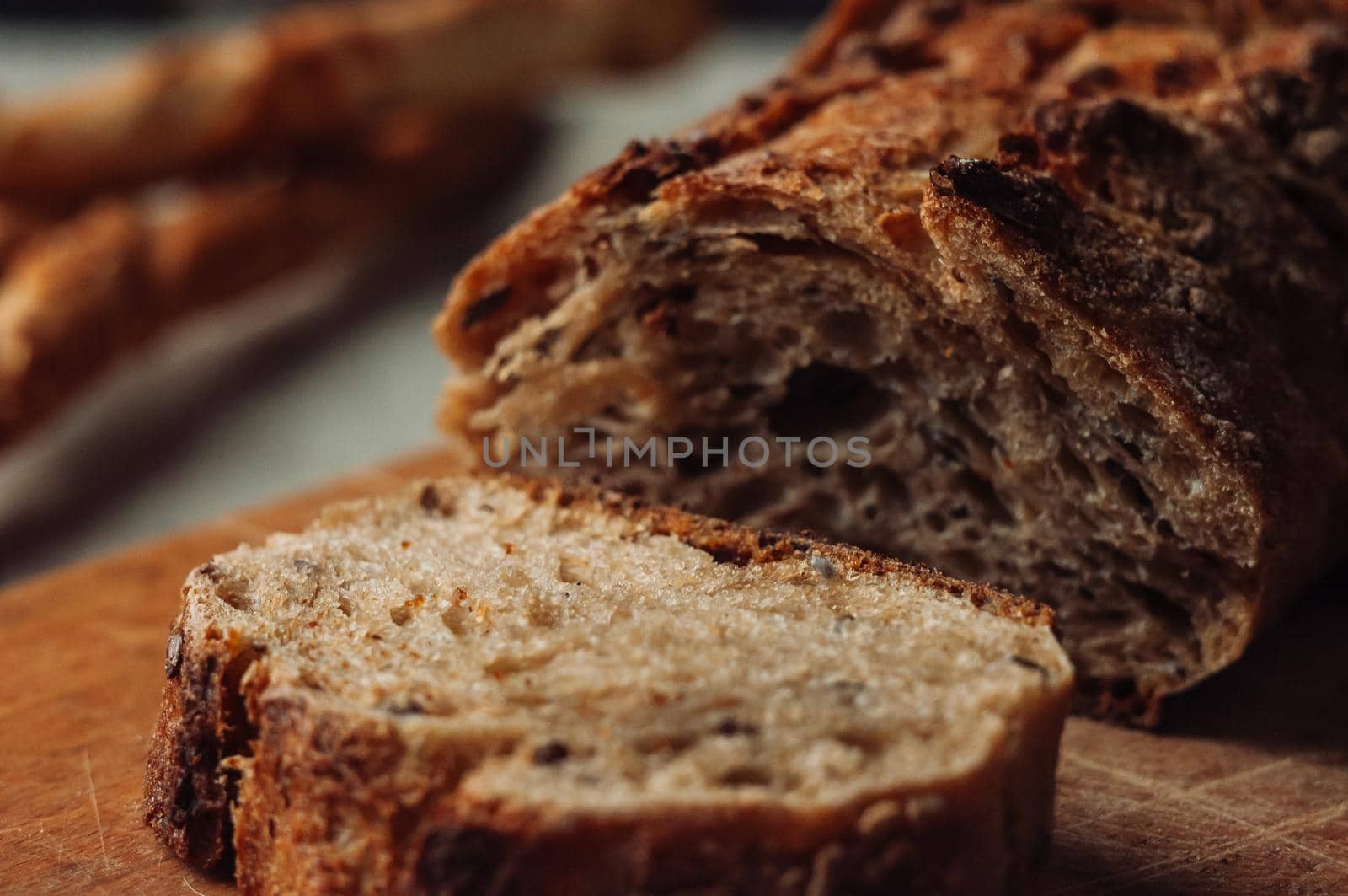 dark yeast-free buckwheat bread in a cut lies on a cutting wooden board on a wooden table next to italian grissini on a linen tablecloth in rustic style. Selective focus. Concept of making breakfast.