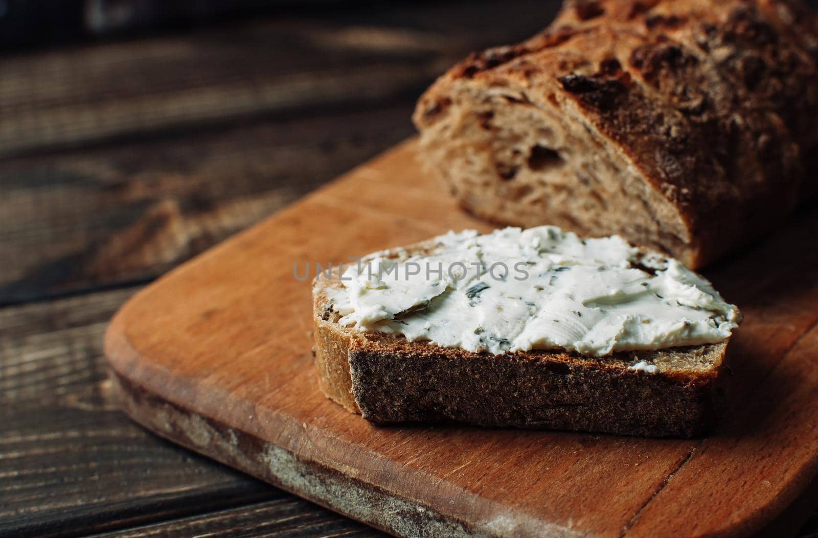 dark bread is spread with cottage cheese with herbs in a cut on a wooden board on a wooden table in a rustic style. Snack and breakfast concept. Selective focus.