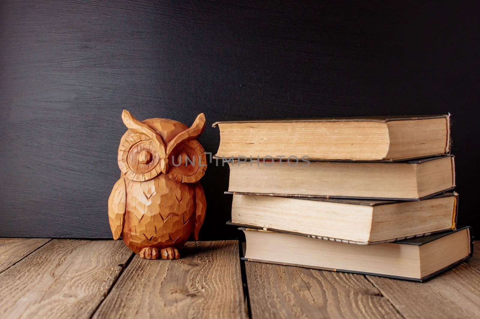 books stacked on a wooden table in a rustic style on the background a school blackboard. Owl on books as a source of wisdom and knowledge. Concept welcome back to school. copy space