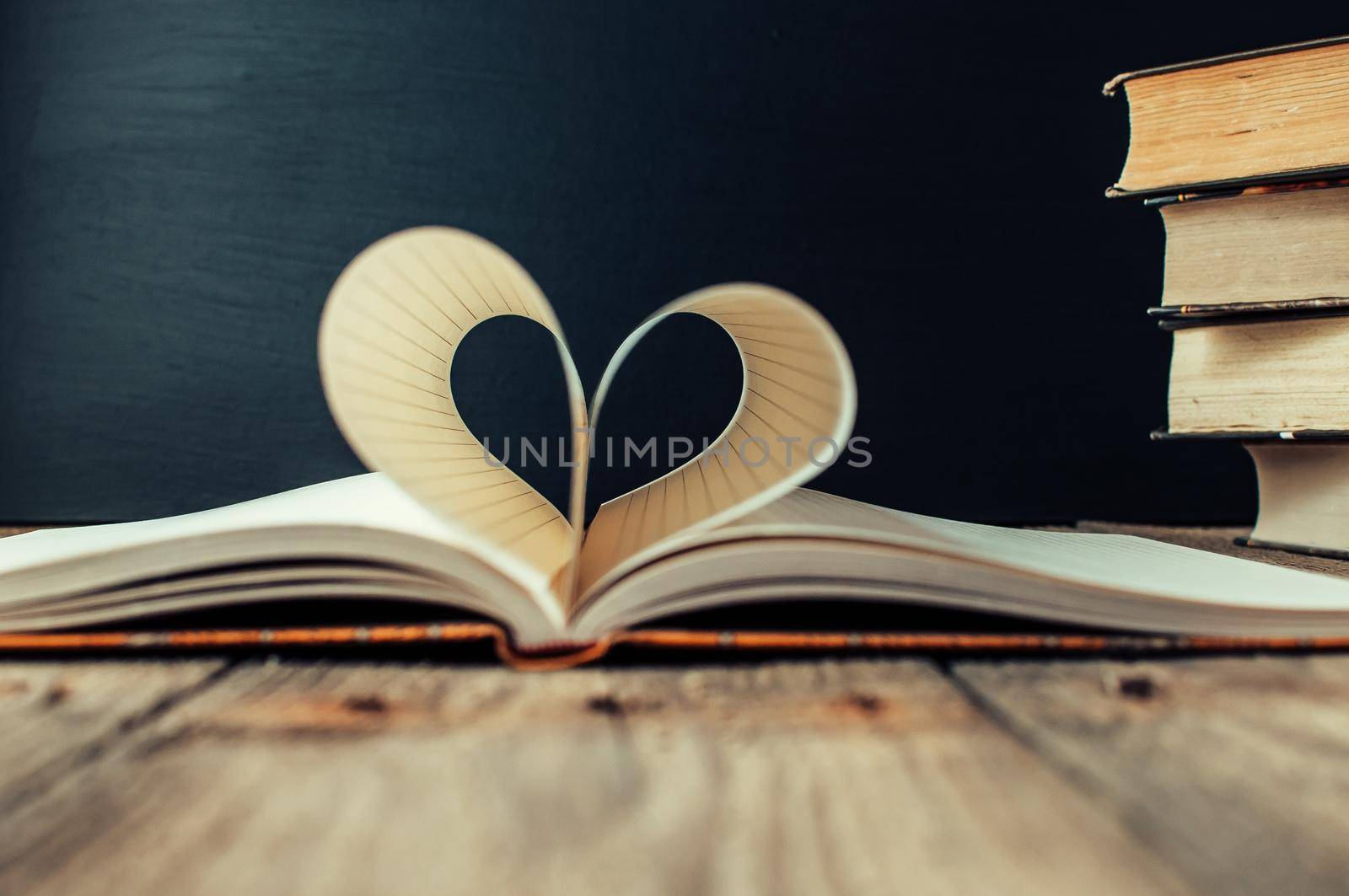 Sheets of a notebook in a cage wrapped in the shape of a heart.In the background is a stack of books and a black board.Education concept.Valentine's Day.Copy space.Rustic and vintage.Concept love.