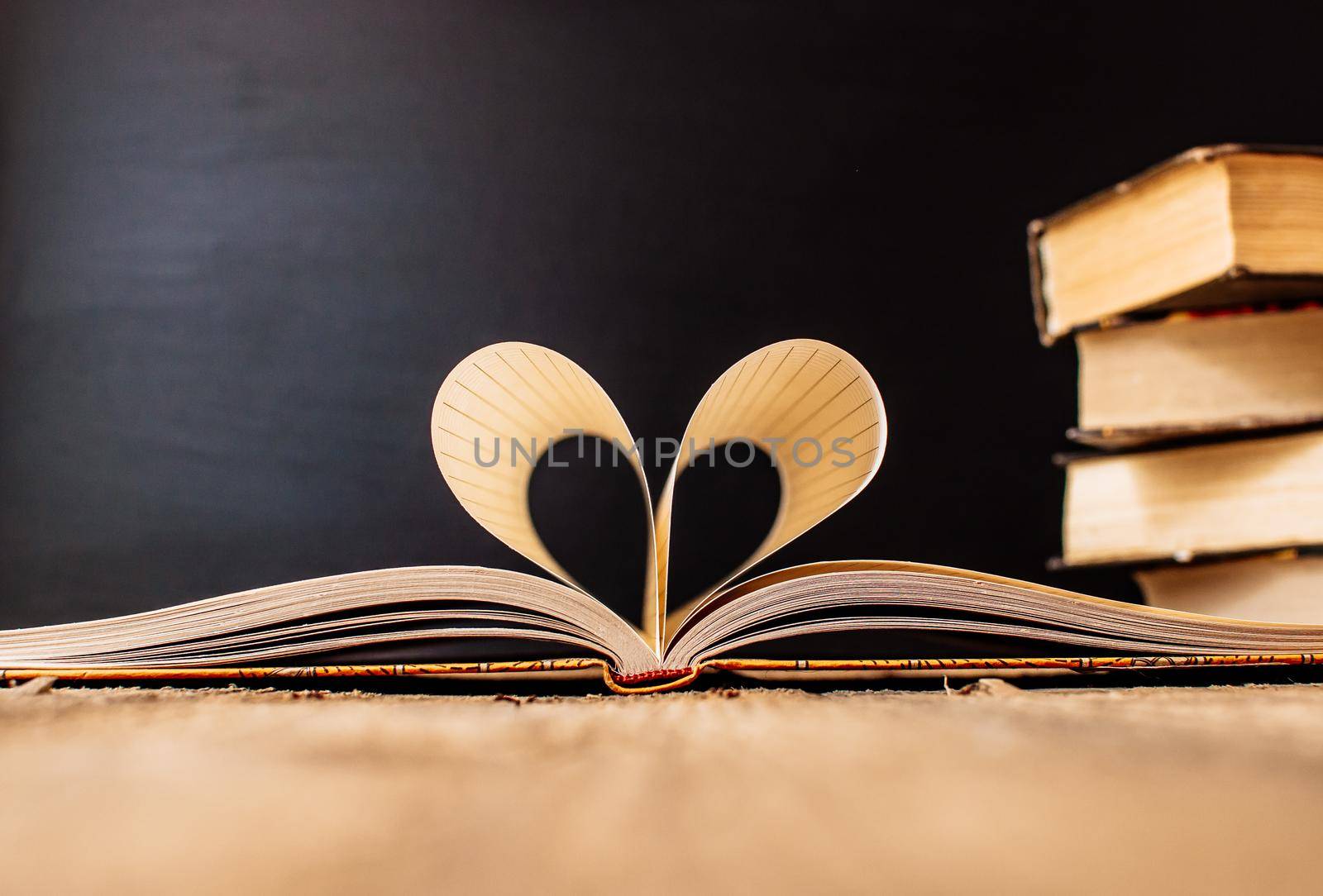 Sheets of a notebook in a cage wrapped in the shape of a heart.In the background is a stack of books and a black board.Education concept.Valentine's Day.Copy space.Rustic and vintage.Concept love.