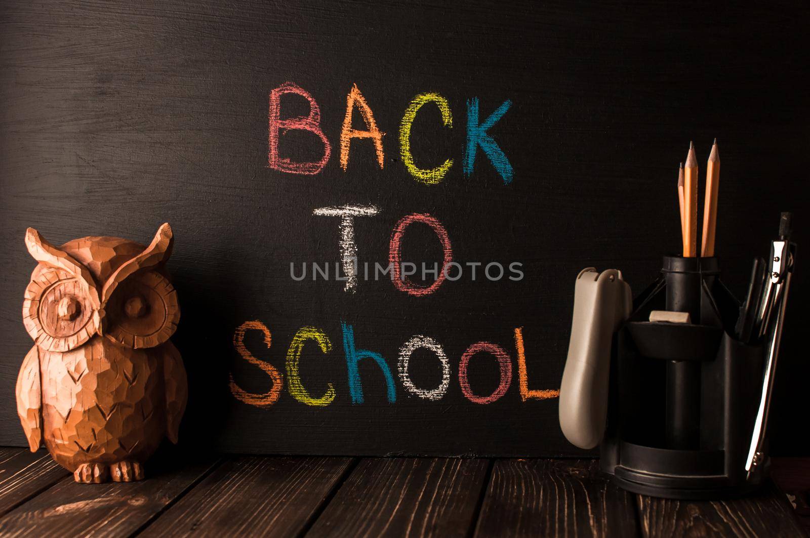 Back to school, the concept of parenting. An assortment of consumables, owl, notebook, pencils, stand for pens. The inscription on the slate black chalk. School supplies on a wooden table, rustic.