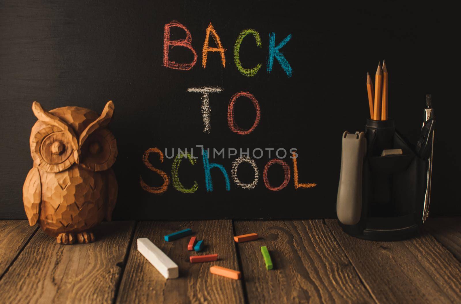 Back to school, the concept of parenting. An assortment of consumables, owl, notebook, pencils, stand for pens. The inscription on the slate black chalk. School supplies on a wooden table, rustic.