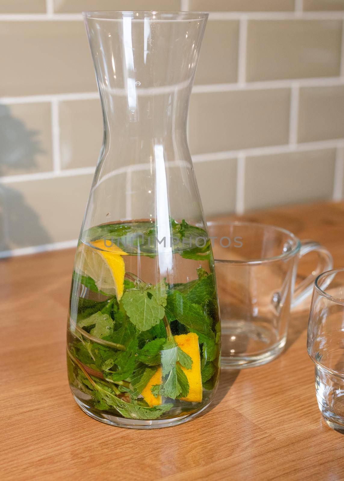 fresh water with lemon and mint in decanter and glass on the table in kitchen