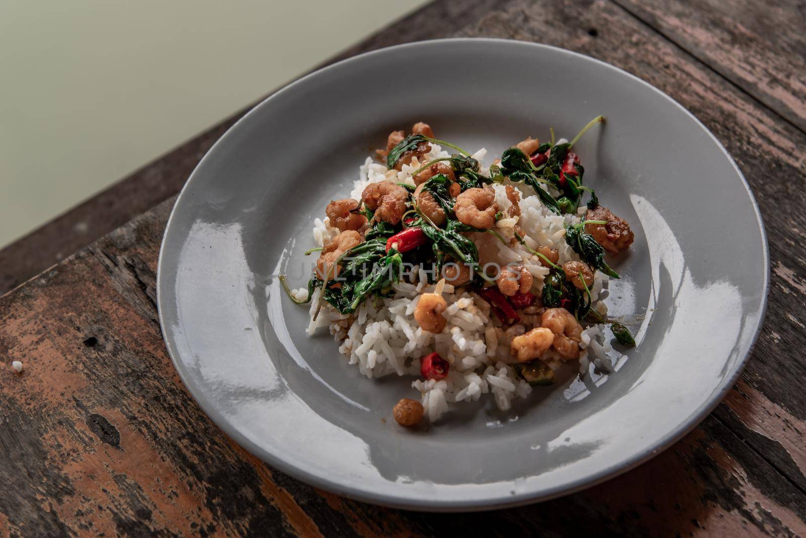 Rice topped with Stir fried thai basil with dwarf prawn served in white dish on wooden table, A world renowned delicacy from Thailand, Selective focus.
