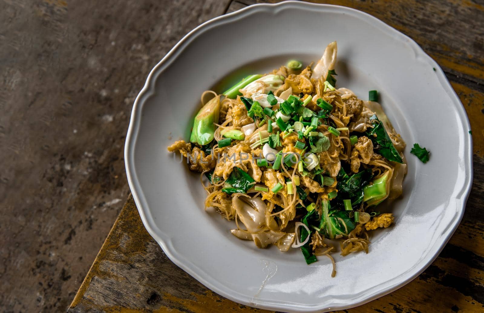 Stir-fried Noodles in Sweet Soy Sauce with Pork ( Pad See-Ew ) served in white dish on wooden table, Thai Style food, Top view, Selective focus.