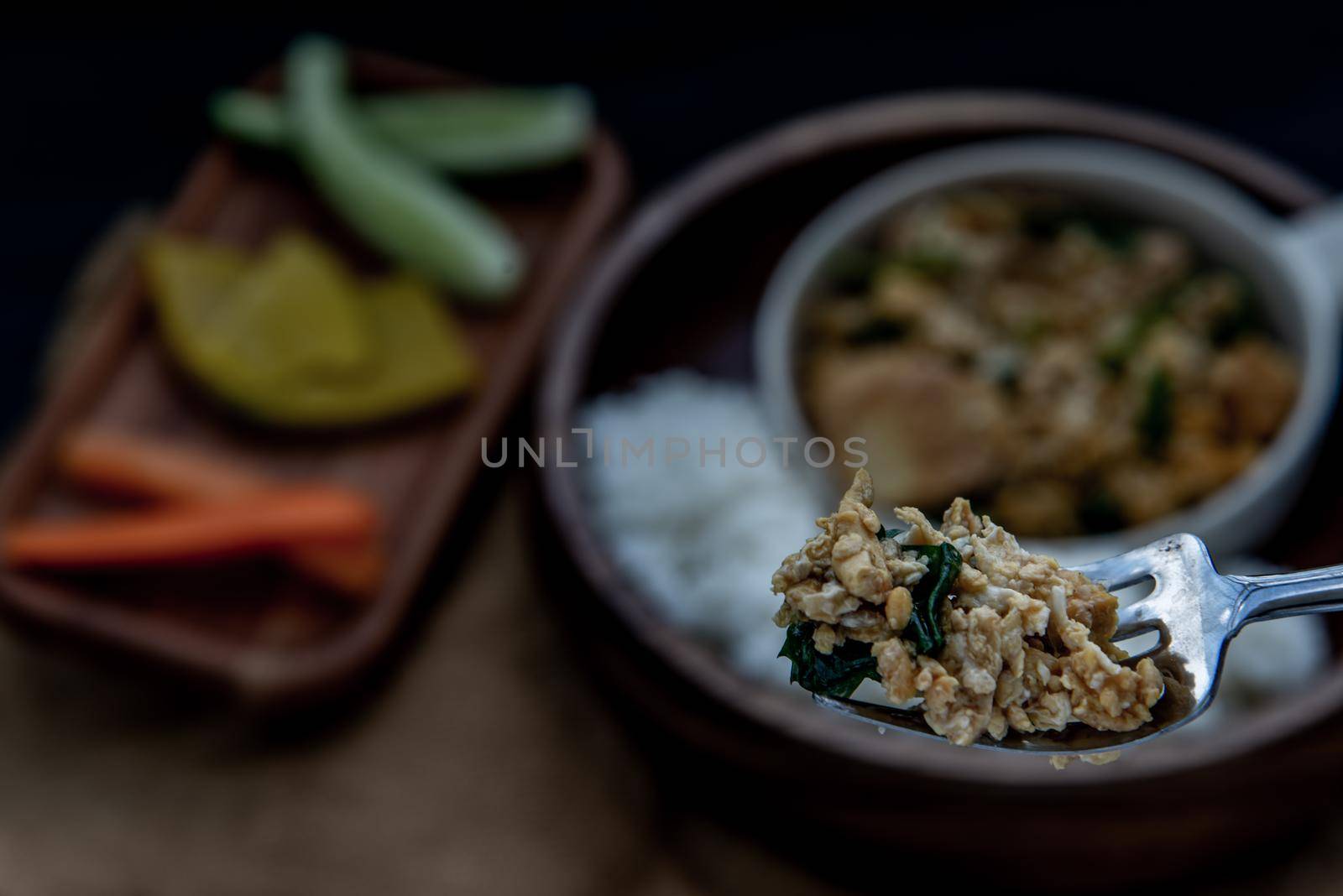 Thai food, The hand is using a fork to scoop Stir fried egg tofu with spring onion with Herbs vegetables served with steamed rice in wooden bowl.