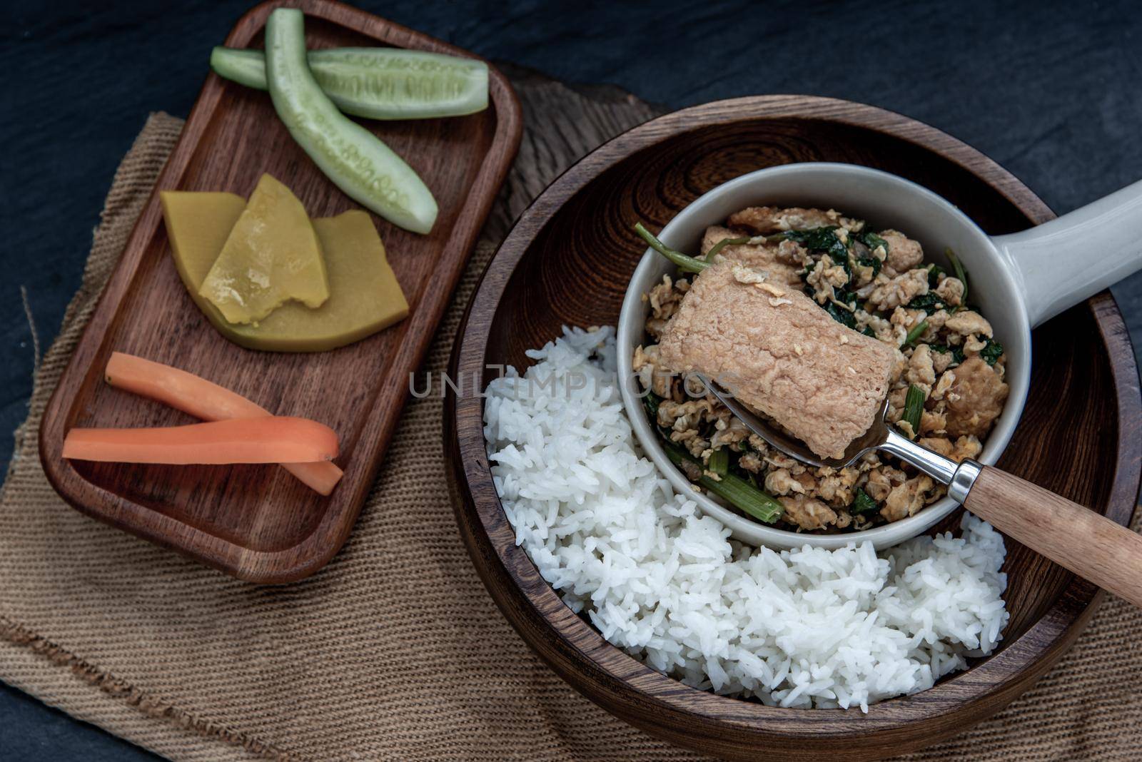 Thai food, The hand is using a fork to scoop Stir fried egg tofu with spring onion with Herbs vegetables served with steamed rice in wooden bowl.