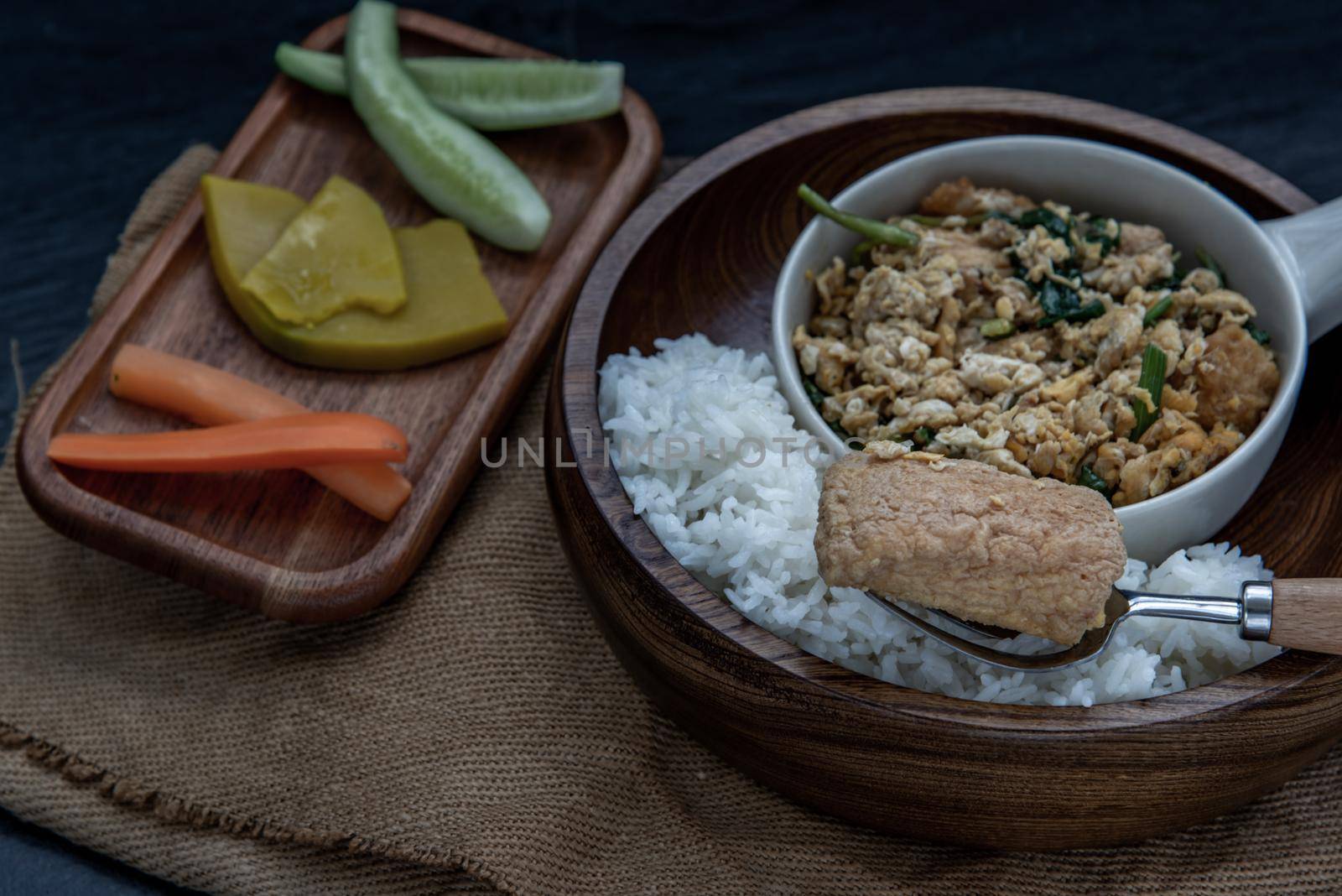 Thai food, The hand is using a fork to scoop Stir fried egg tofu with spring onion with Herbs vegetables served with steamed rice in wooden bowl.