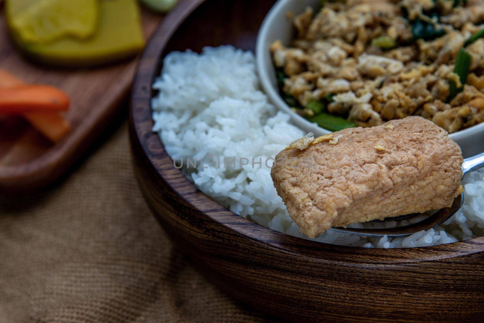 Thai food, Close-up of The hand is using a fork to scoop Stir fried egg tofu with spring onion with Herbs vegetables served with steamed rice in wooden bowl.