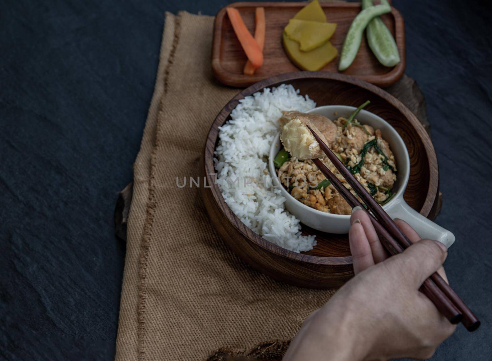 Thai food, The hand is using chopsticks to pick up  Stir fried egg tofu with spring onion with Herbs vegetables served with steamed rice in wooden bowl.
