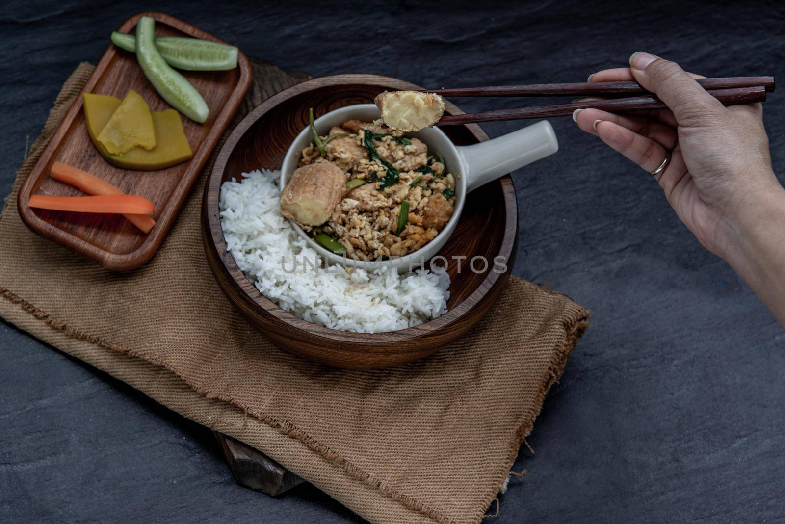 Thai food, The hand is using chopsticks to pick up  Stir fried egg tofu with spring onion with Herbs vegetables served with steamed rice in wooden bowl.
