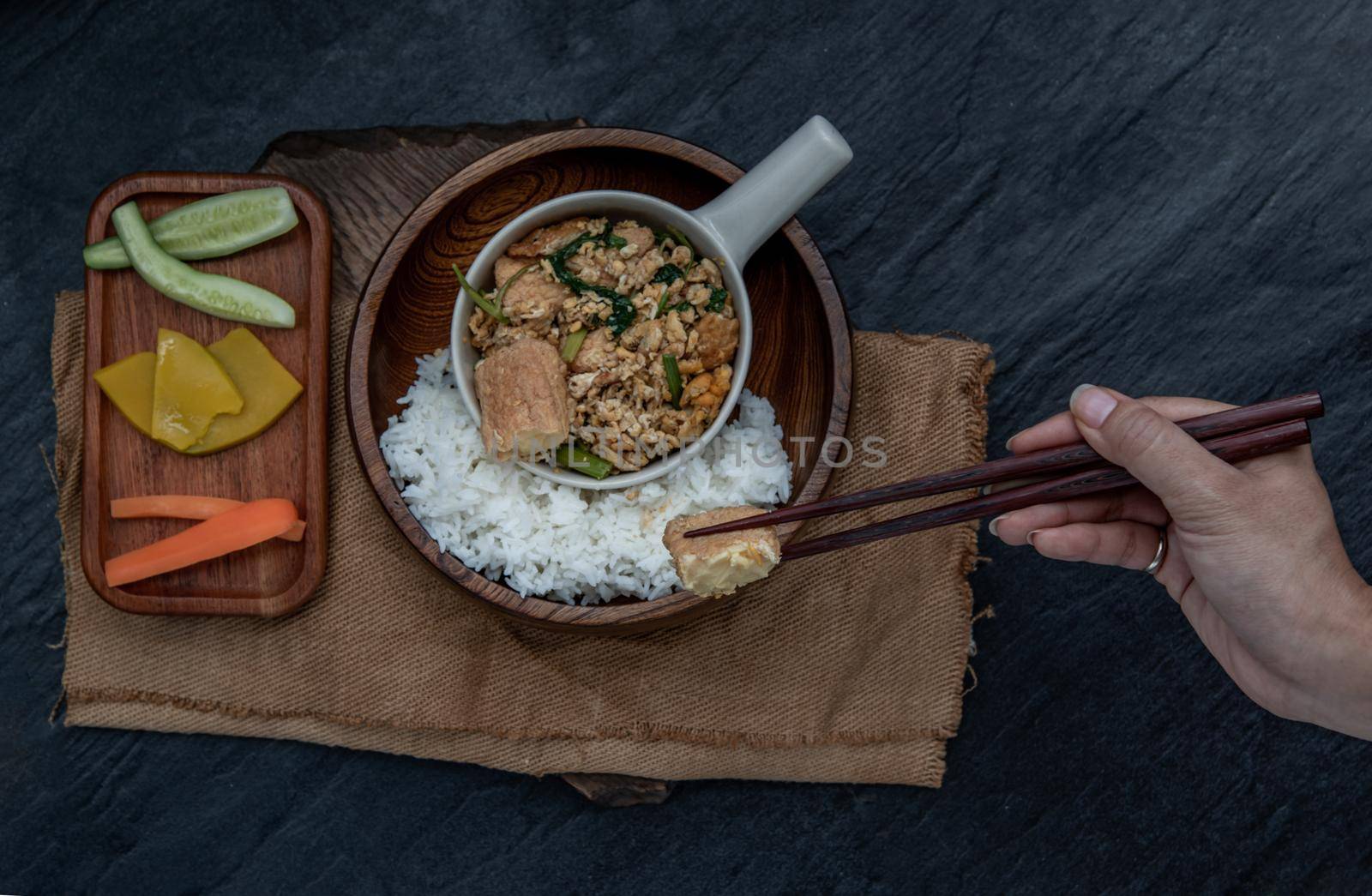 Thai food, The hand is using chopsticks to pick up  Stir fried egg tofu with spring onion with Herbs vegetables served with steamed rice in wooden bowl.