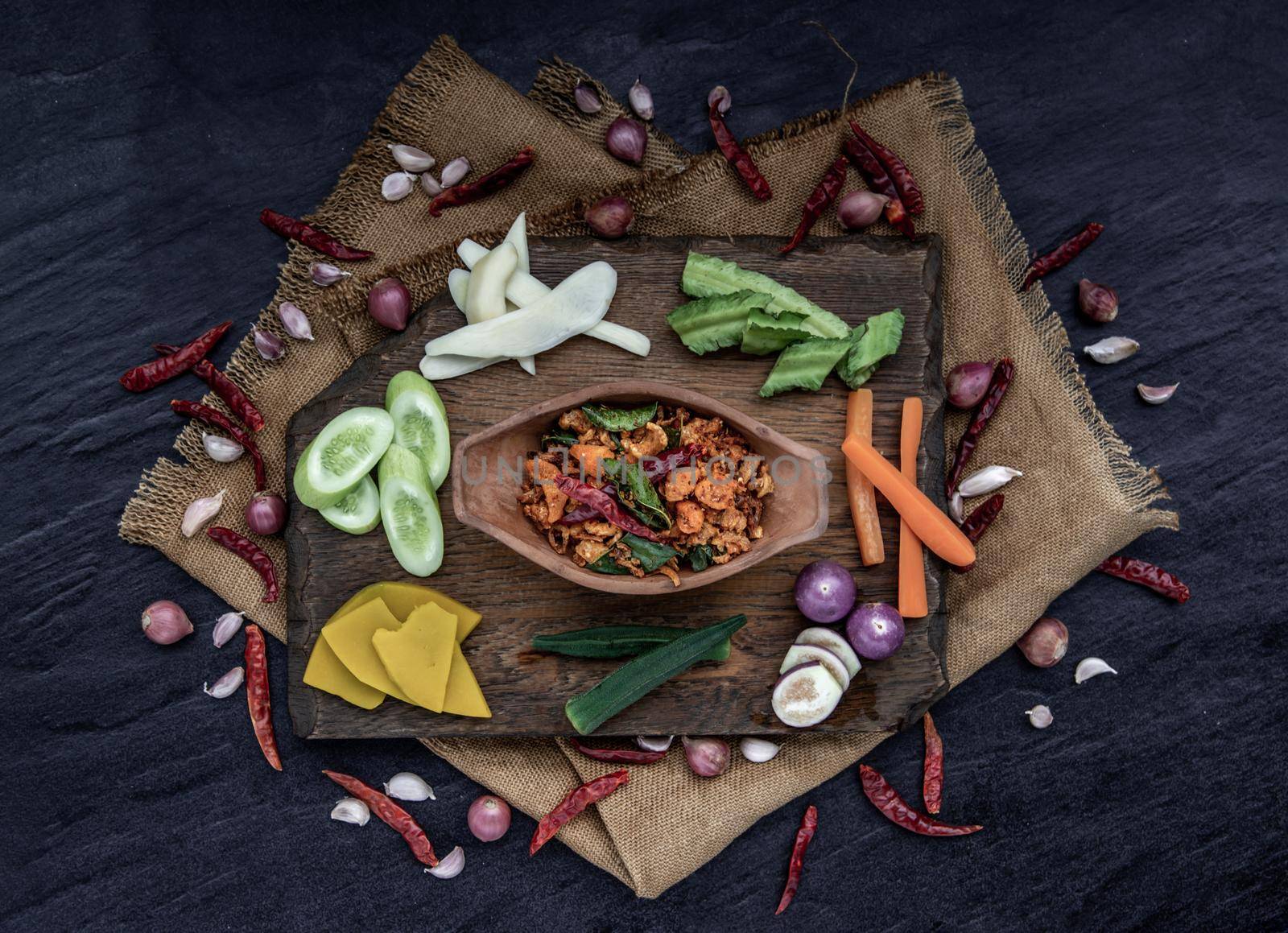 Pork Crackling Chili Paste with fried kaffir lime leaves with the ingredient and fresh vegetables on wood background, Top view.