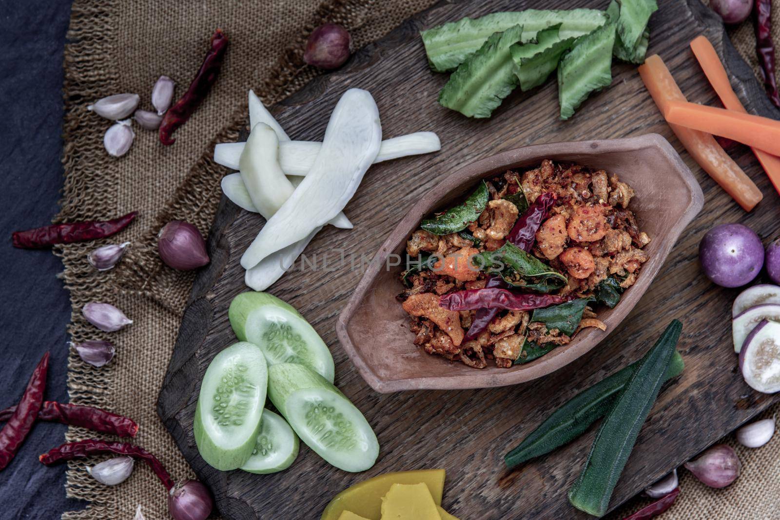 Pork Crackling Chili Paste with fried kaffir lime leaves with the ingredient and fresh vegetables on wood background, Top view.