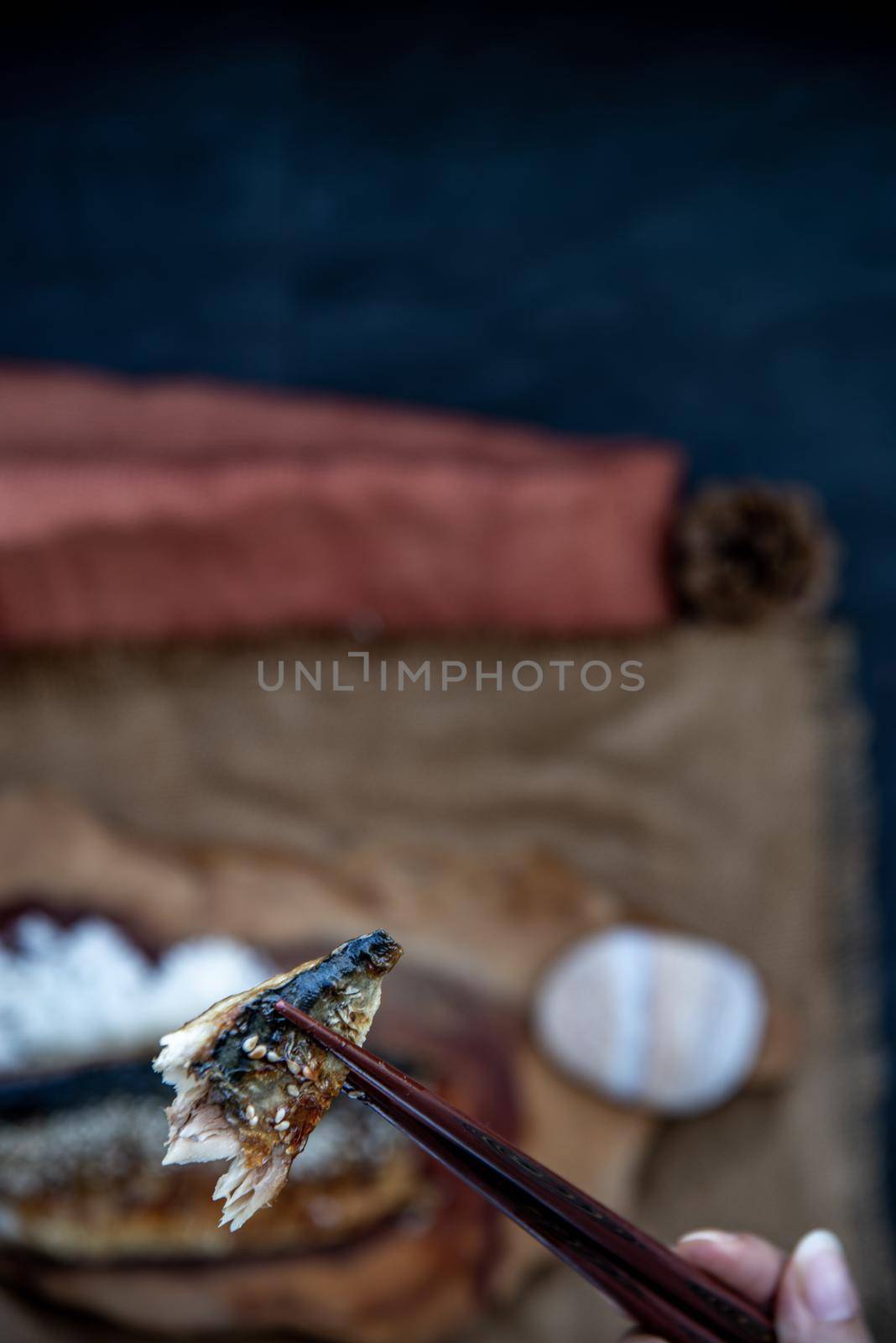 The hand is using chopsticks to pick up saba fish grilled on rice with teriyaki sauce on a sackcloth background, Japanese style.
