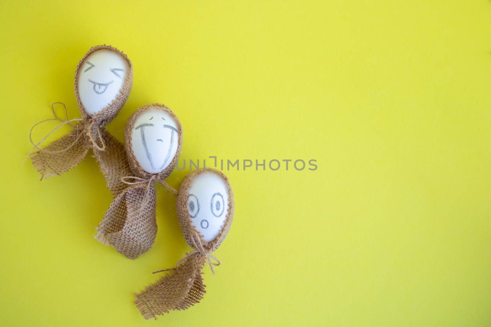 Three white eggs with funny faces in sackcloth on a yellow background. Easter Concept. Space for text.