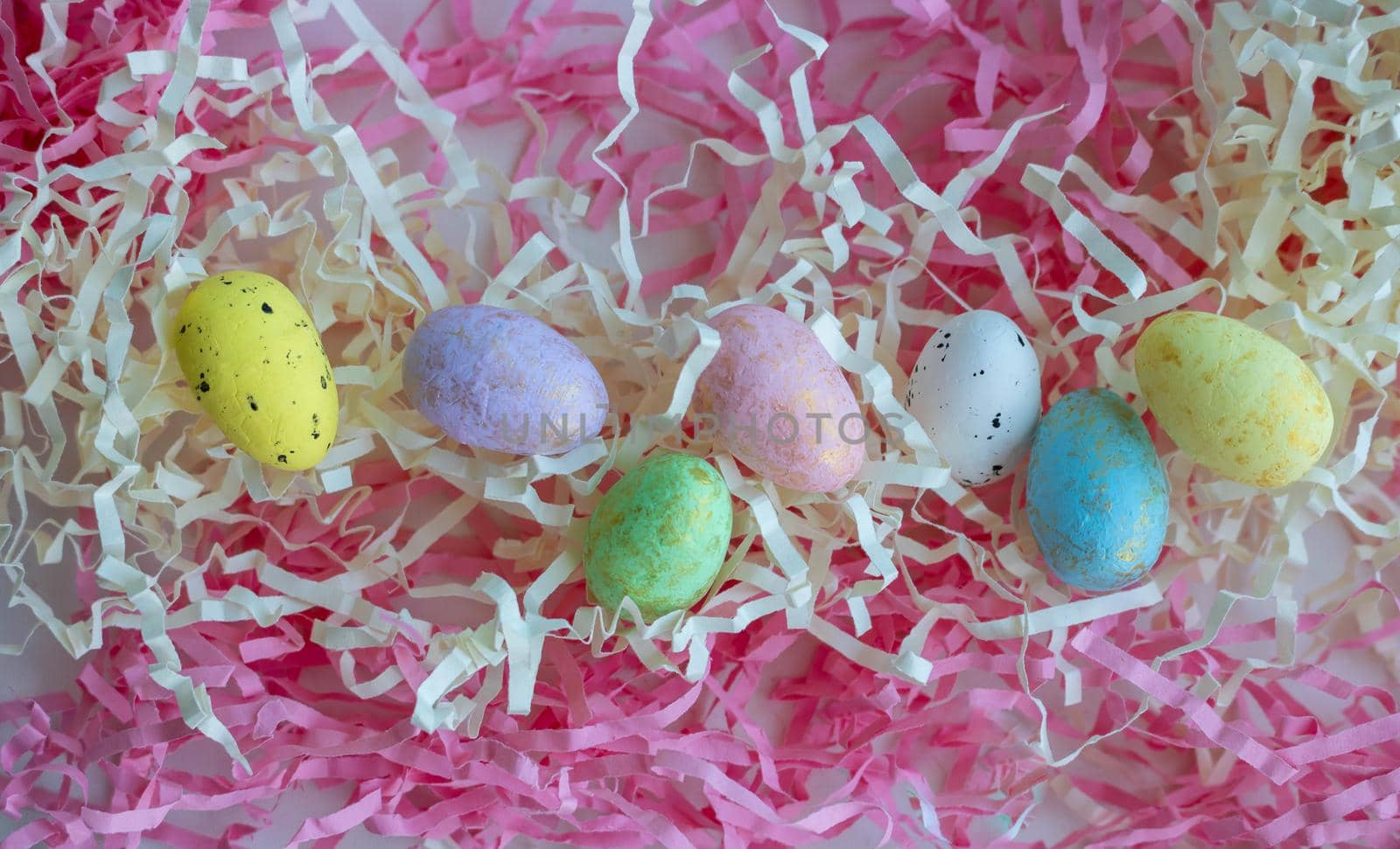 Colorful eggs on a background of pink and white paper tinsel. Easter concept.