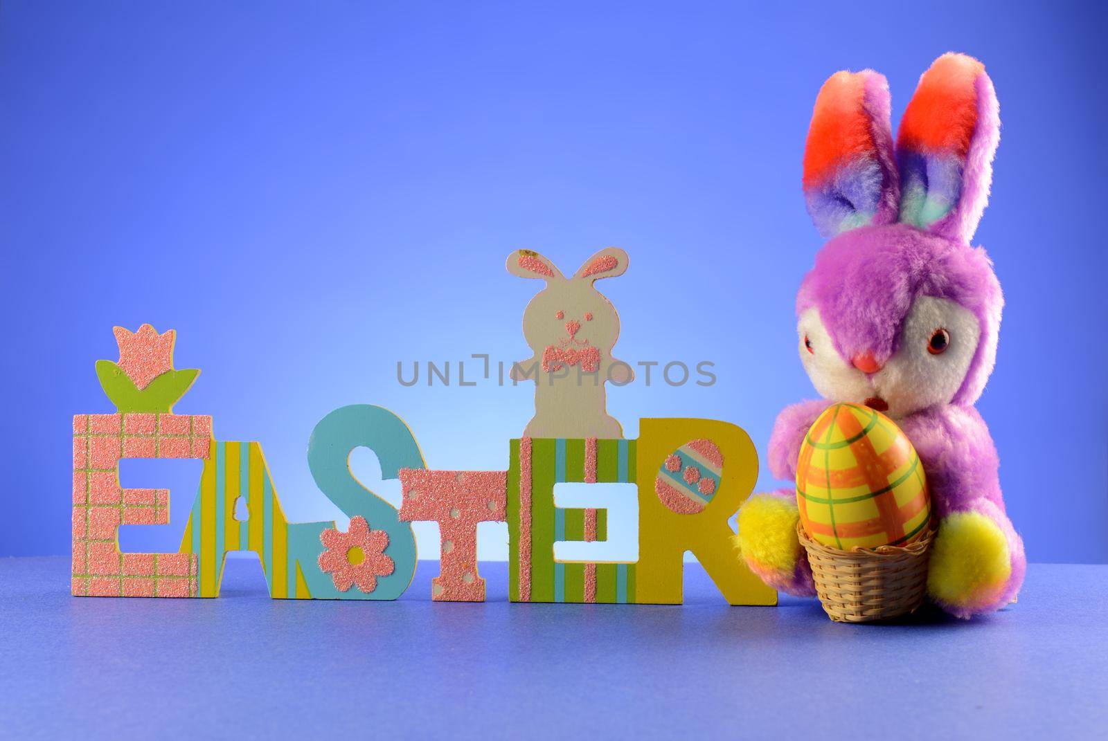 A festive holiday sign for Easter with a plush bunny over a blue background.