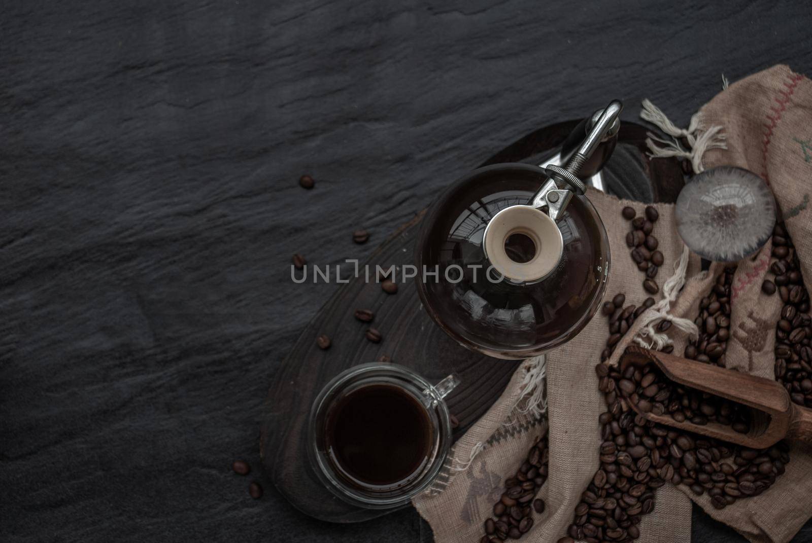 Coffee style, Cup of coffee and coffee beans roating with old wooden scoop and coffee beans around on the wooden and dark stone background. Top view with copy space for your text.