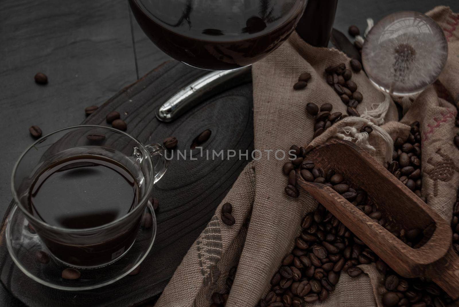 Coffee style, Cup of coffee and coffee beans roating with old wooden scoop and coffee beans around on the wooden and dark stone background. Close-up.