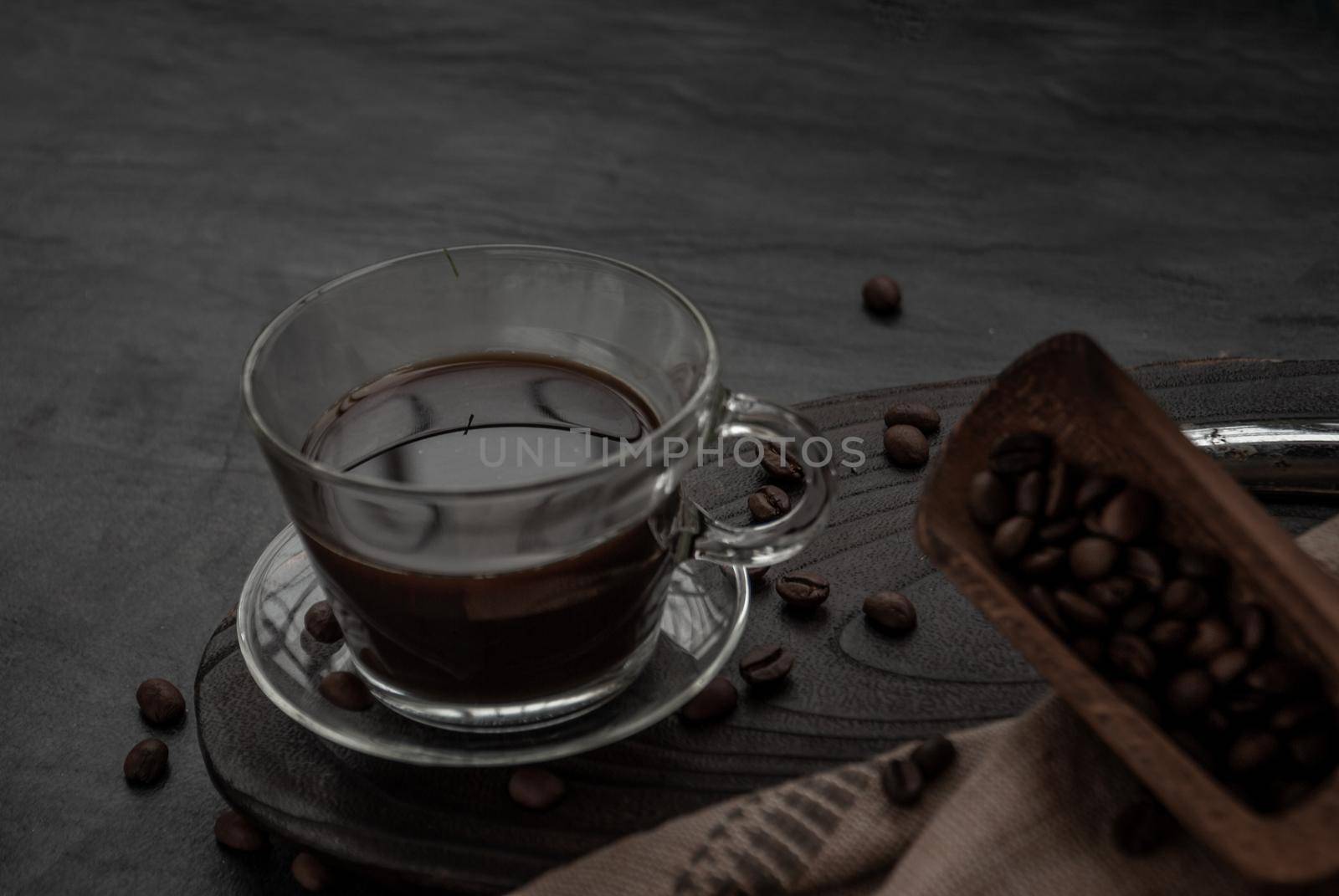 Coffee style, Cup of coffee and coffee beans roating with old wooden scoop and coffee beans around on the wooden and dark stone background. Oblique view from the top with copy space for your text.