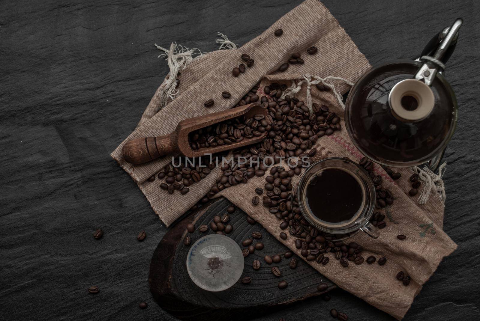 Coffee style, Cup of coffee and coffee beans roating with old wooden scoop and coffee beans around on the wooden and dark stone background. Top view with copy space for your text.