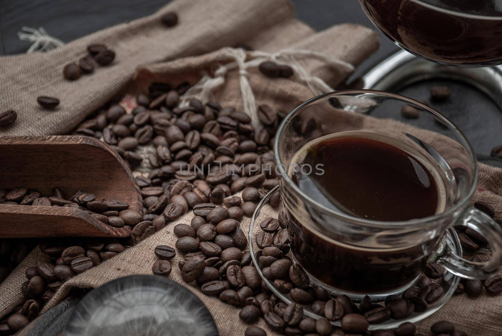 Coffee style, Cup of coffee and coffee beans roating with old wooden scoop and coffee beans around on the wooden and dark stone background. Close-up.