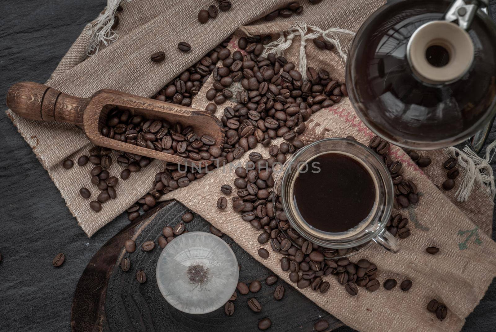 Coffee style, Cup of coffee and coffee beans roating with old wooden scoop and coffee beans around on the wooden and dark stone background. Top view.