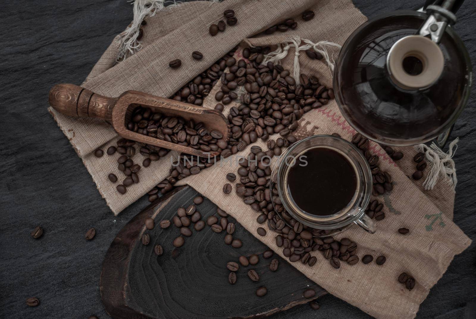 Coffee style, Cup of coffee and coffee beans roating with old wooden scoop and coffee beans around on the wooden and dark stone background. Top view, Selective focus.