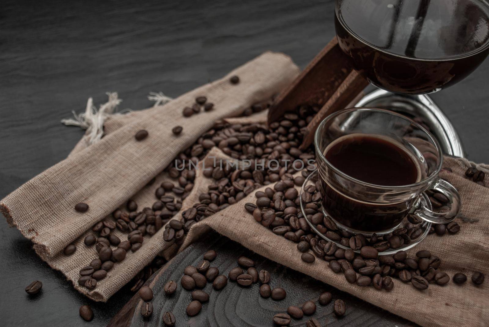 Coffee style, Cup of coffee and coffee beans roating with old wooden scoop and coffee beans around on the wooden and dark stone background. Oblique view from the top with copy space for your text.
