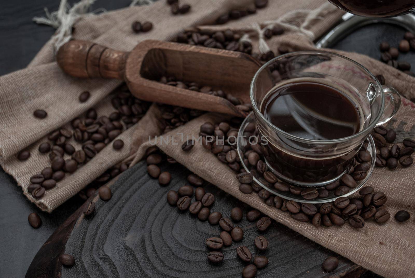 Coffee style, Cup of coffee and coffee beans roating with old wooden scoop and coffee beans around on the wooden and dark stone background. Close-up.