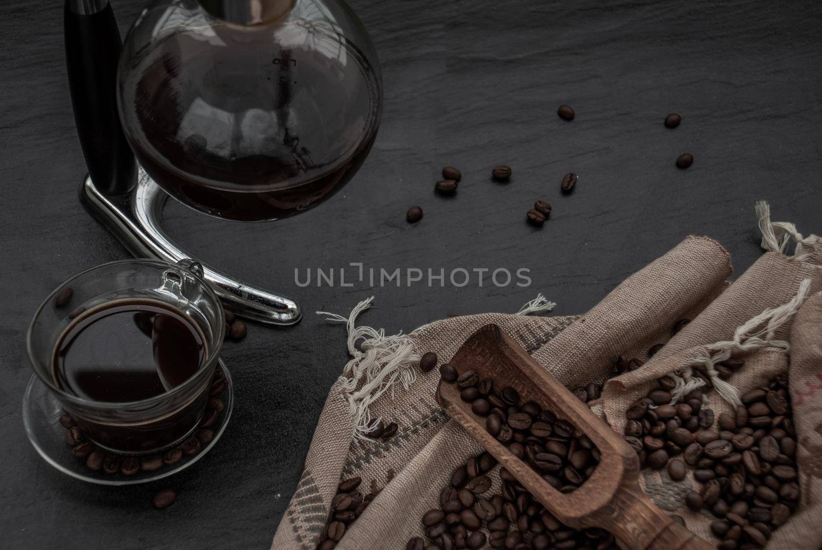 Coffee style, Cup of coffee and coffee beans roating with old wooden scoop and coffee beans around on the wooden and dark stone background. Oblique view from the top with copy space for your text.
