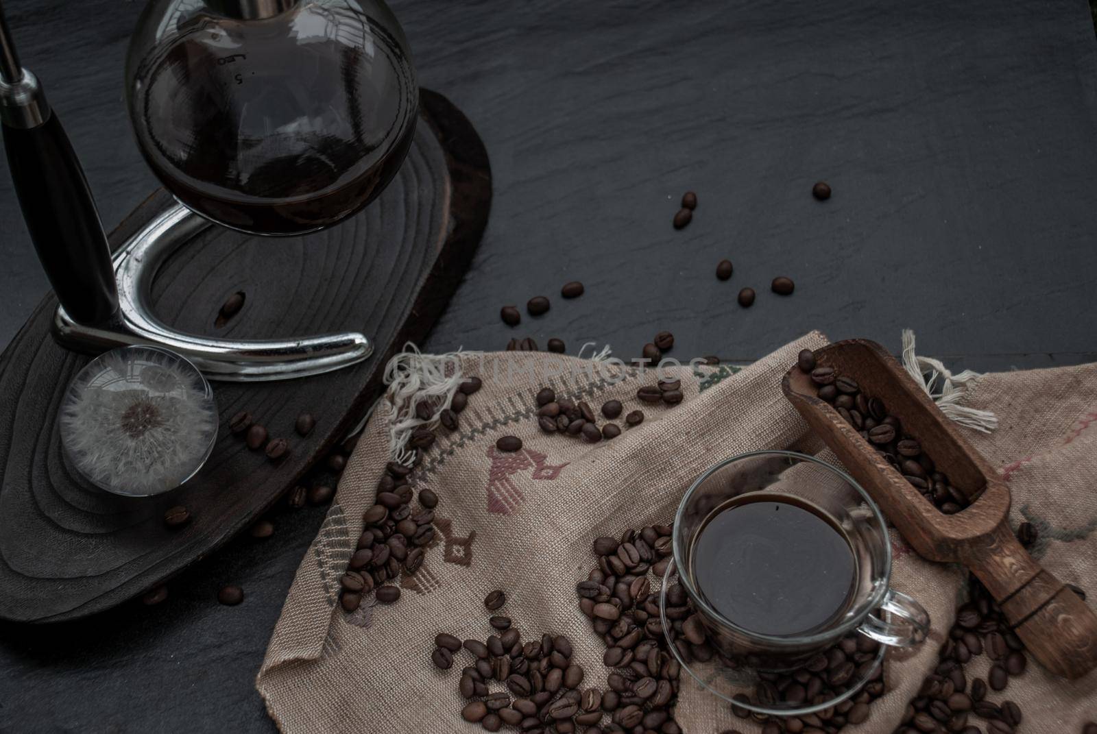Coffee style, Cup of coffee and coffee beans roating with old wooden scoop and coffee beans around on the wooden and dark stone background. Oblique view from the top with copy space for your text.