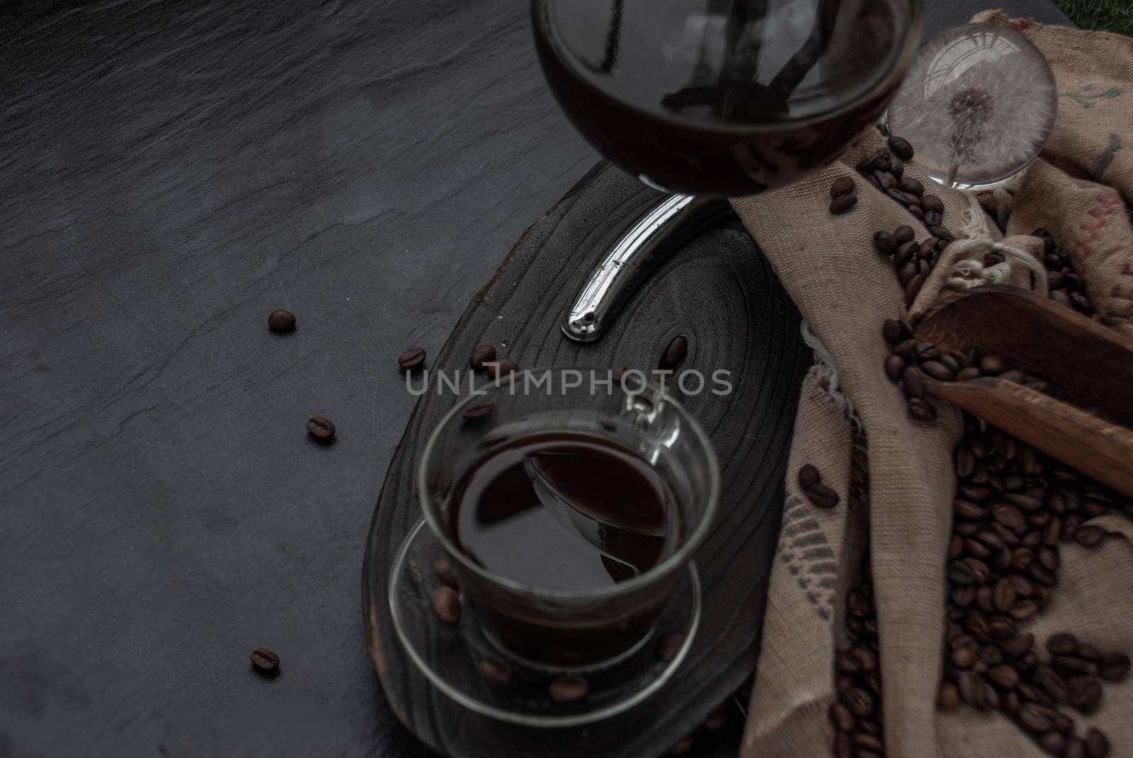 Coffee style, Cup of coffee and coffee beans roating with old wooden scoop and coffee beans around on the wooden and dark stone background. Oblique view from the top with copy space for your text.