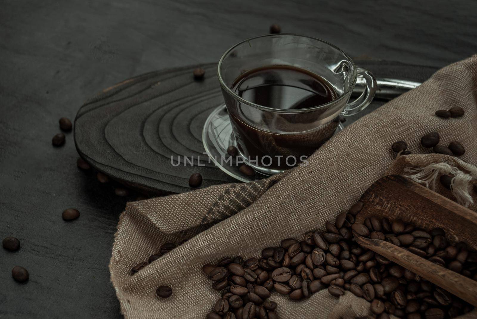 Coffee style, Cup of coffee and coffee beans roating with old wooden scoop and coffee beans around on the wooden and dark stone background. Oblique view from the top with copy space for your text.