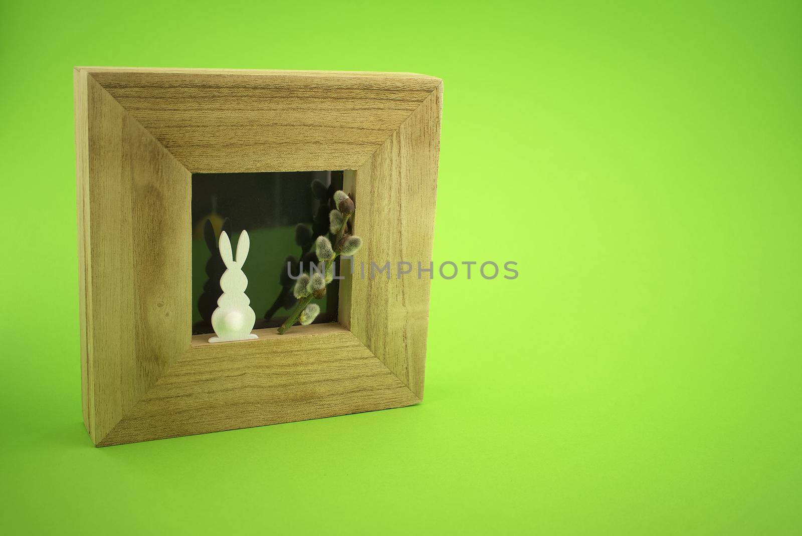 Easter Decoration with photo frame, Easter Rabbit figure and pussy willow branch over a green background. Happy Easter card concept with free copy space for text