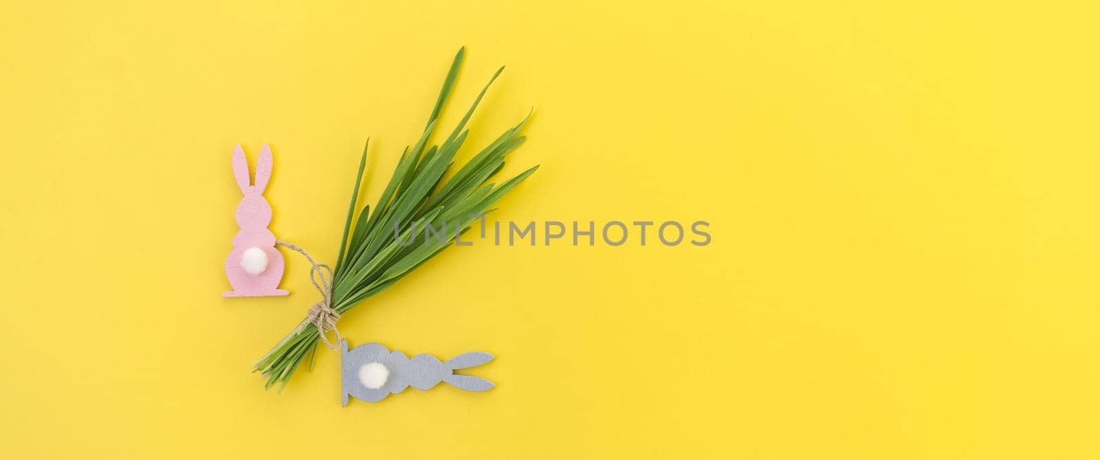 Minimalistic Easter card or banner with Easter Rabbit figures and bundle of wheat seedlings tied with linen twine on yellow color background with copy space for your text