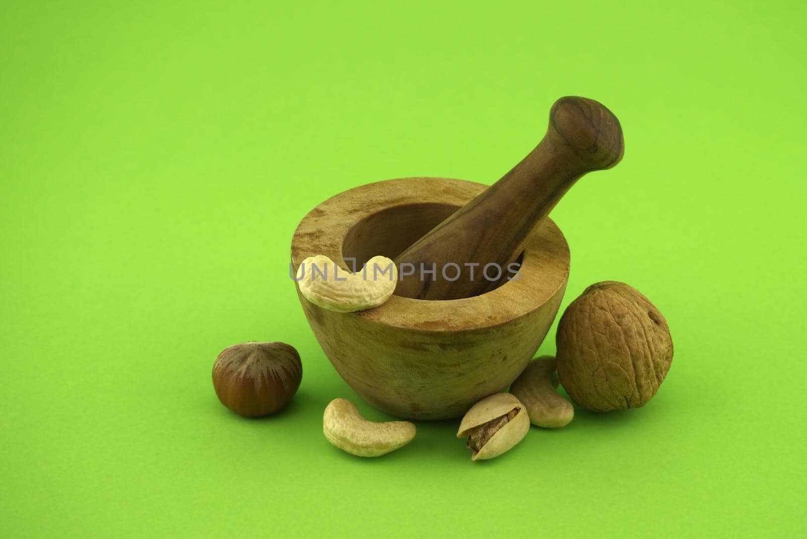 Wooden rustic-style mortar and pestle and various nuts over green background with free space for text. Spices and herb grinder