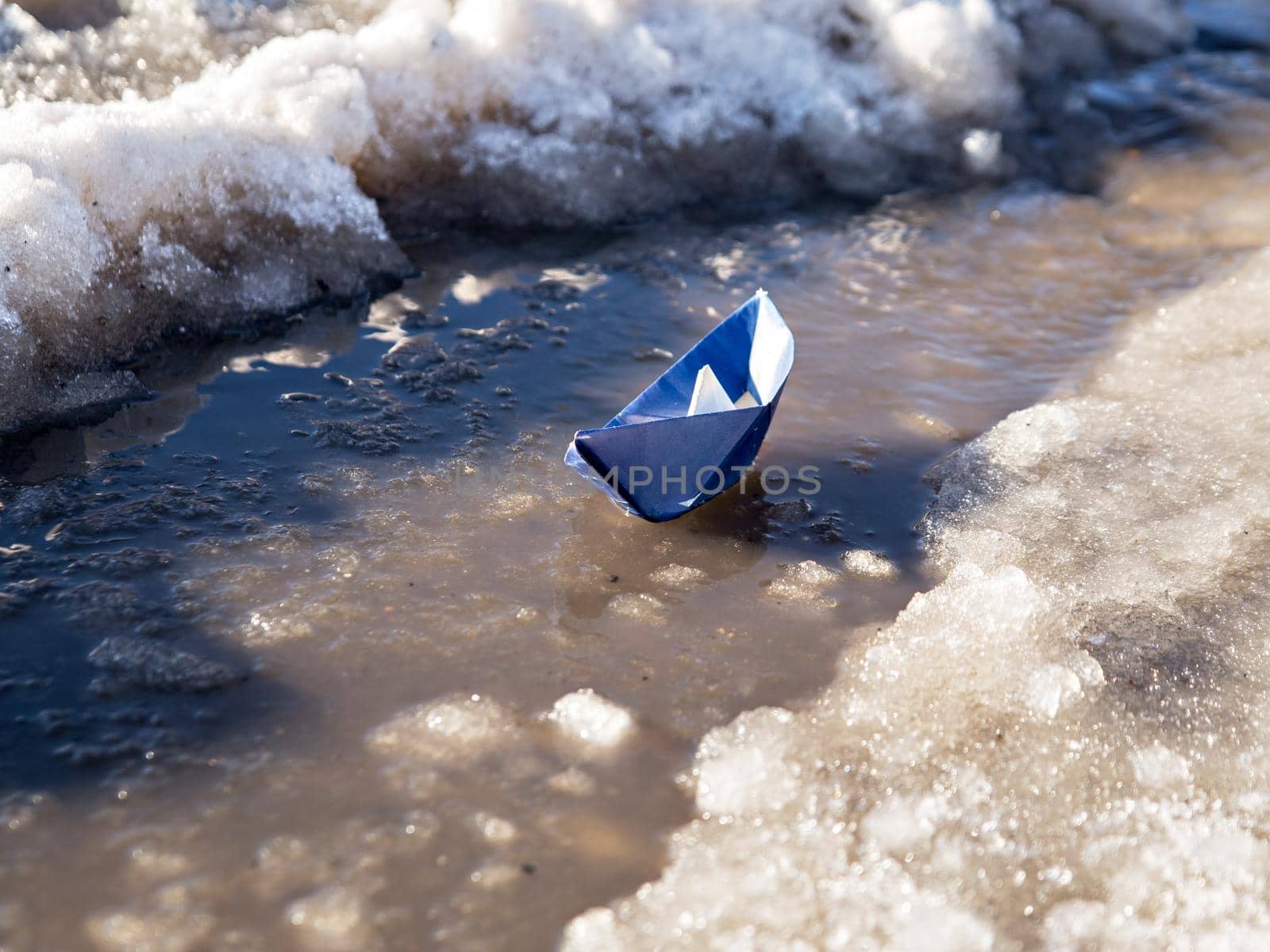 Paper boat floats on water amid melting snow.