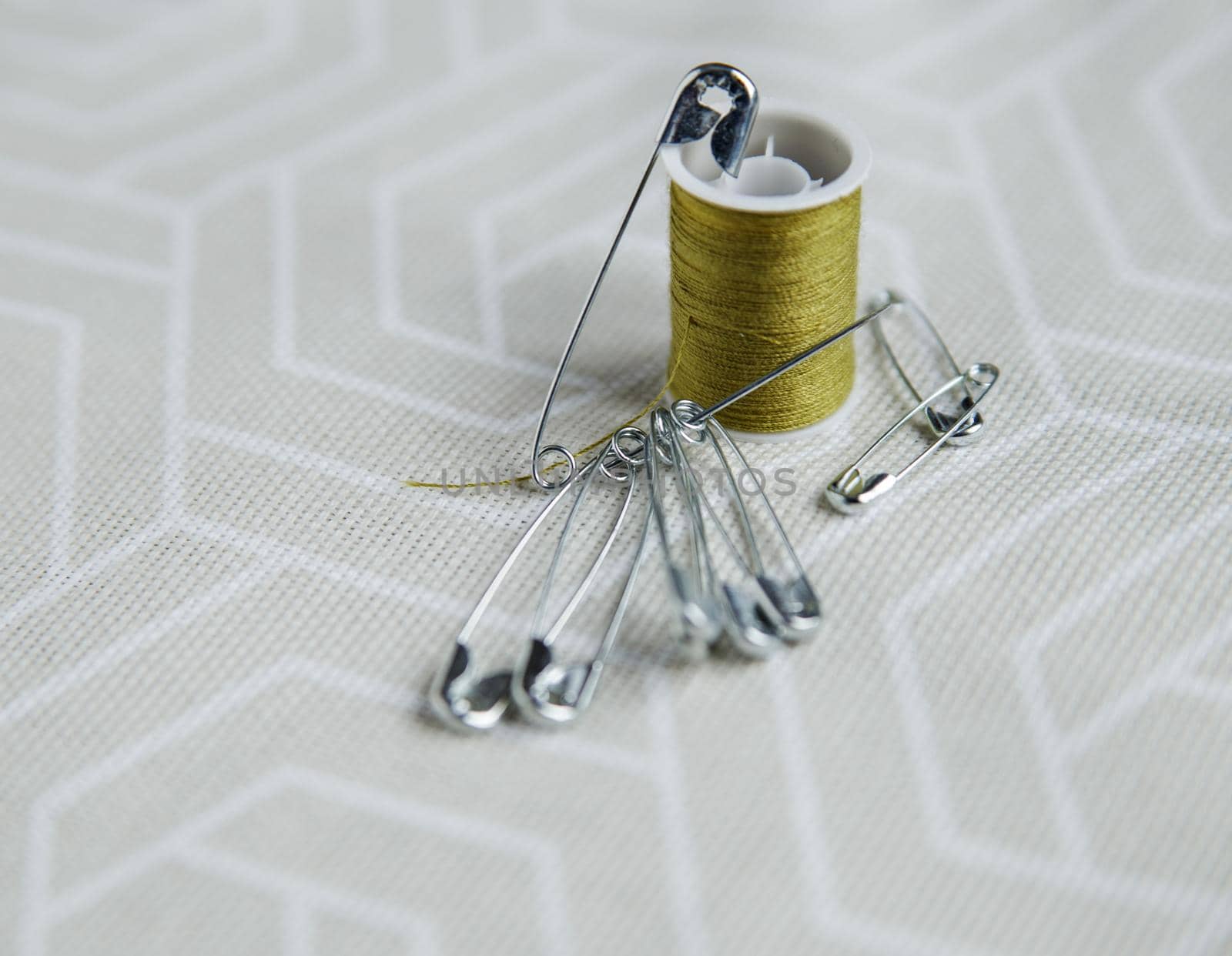 Tailor pins and spool of green thread on gray fabric.Selective focus