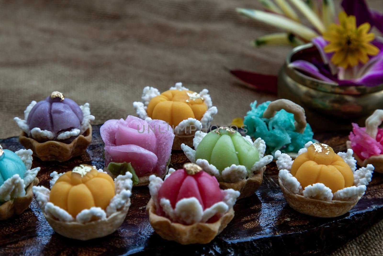 A variety of elegantly beautiful Thai Desserts (Khanom Wan Thai) colorful variations serving in a dark wooden, The bites in gold color and different flower shapes, Thai dessert, Auspicious dessert, Oblique view from the top.