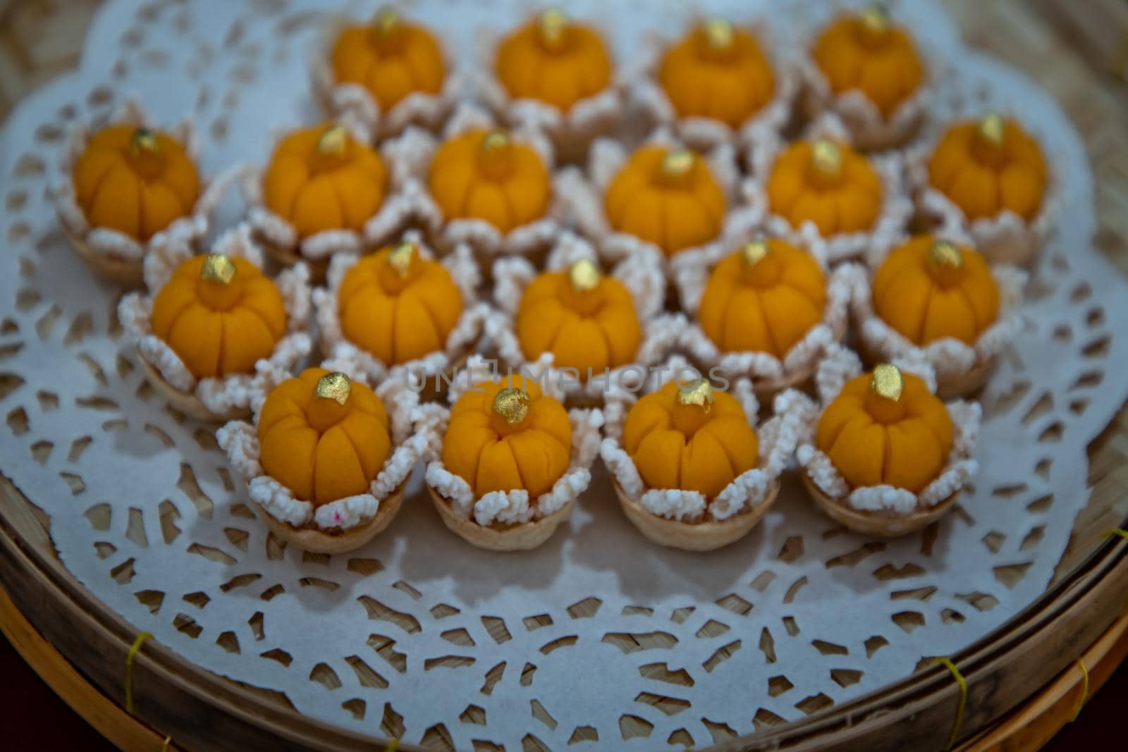 Elegantly beautiful Thai Desserts (Khanom Wan Thai) serving in a Bamboo basket hand made, The bites in gold color and different flower shapes.Thai dessert, Auspicious dessert, Selective focus.