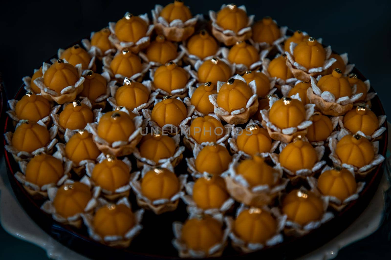 Elegantly beautiful Thai Desserts (Khanom Wan Thai) serving on a wooden background, The bites in gold color and different flower shapes.Thai dessert, Auspicious dessert.